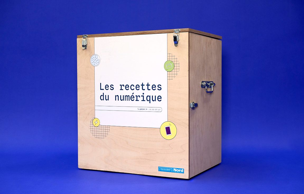 Malle en bois clair sous forme d'un cube avec un habillage sur le devant "Les recettes du numérique".